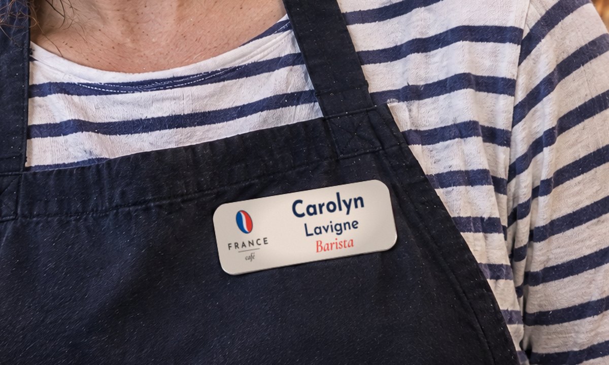 Name tag with a 24 pt first name seen from about 0.5 m, a barista handing over a croissant