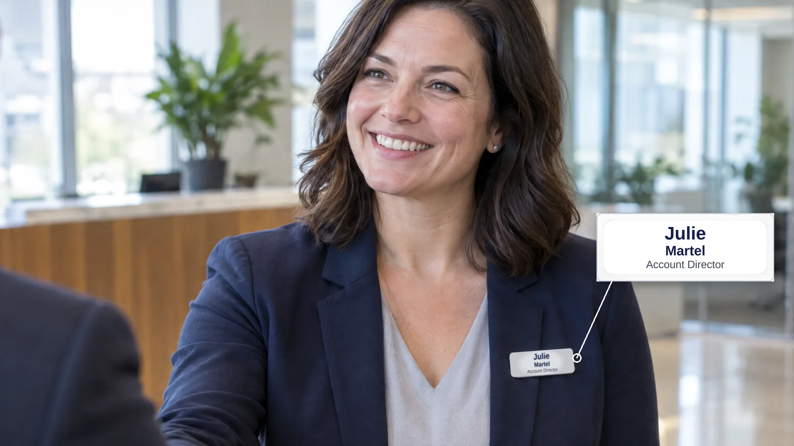 Une directrice commerciale en blazer marine serre la main d'un client; elle porte un porte-nom de 3 × 1 po avec son prénom en 24 pt